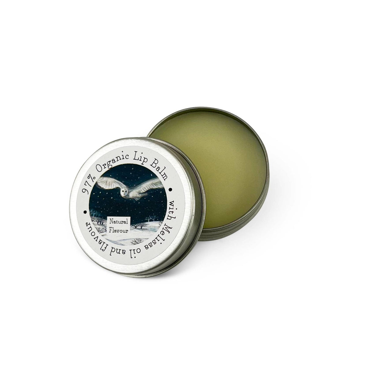 An open round metal tin of organic lip balm showing the pale yellow-green balm inside, with the lid placed beside it. The lid has a printed label featuring a night sky, an owl, and the text '97% Organic Lip Balm' and 'Nature's Flavour'.